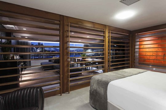Dormitorio moderno con cama blanca, cortinas de madera y vista panorámica nocturna — proyecto Quartos, por Xico Diniz