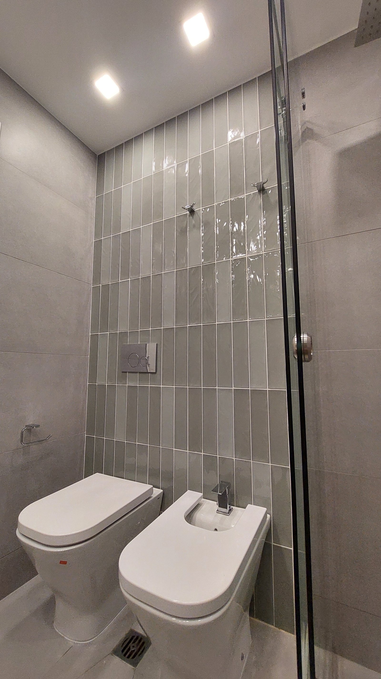 Baño moderno con bidet e inodoro, azulejos verticales y ducha de vidrio — proyecto FLORES, por Arquitecta, en Flores