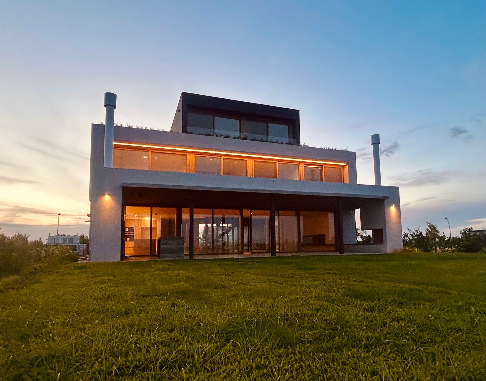 Fachada moderna de hormigón blanco con grandes ventanales — proyecto Casa Puentes, por Guerrero Arquitectos, en Rincón de Milberg