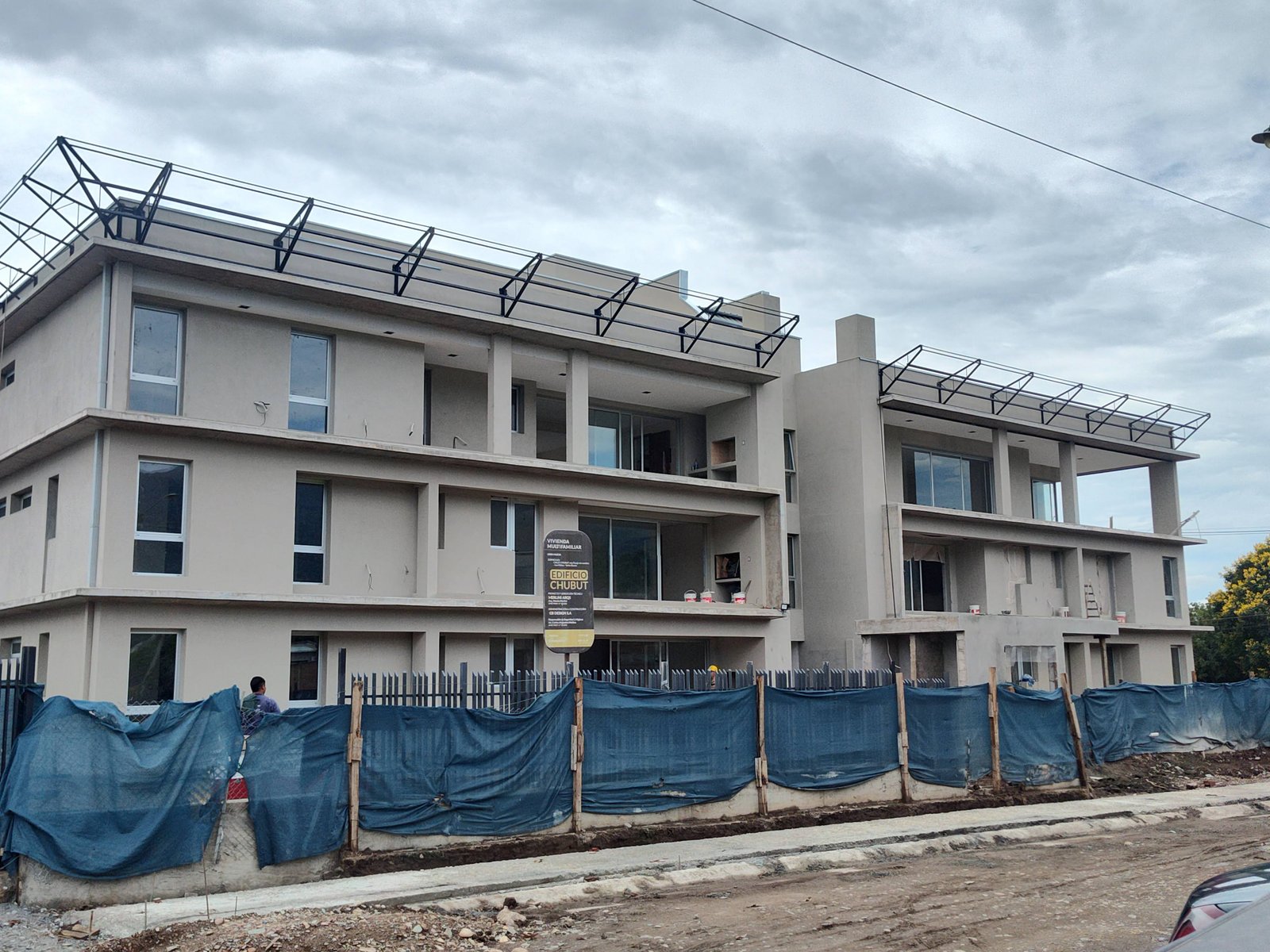 Edificio residencial moderno en construcción con lonas azules — proyecto EDIFICIO CHUBUT, por HMCONSTRUCCIONES, en Chubut