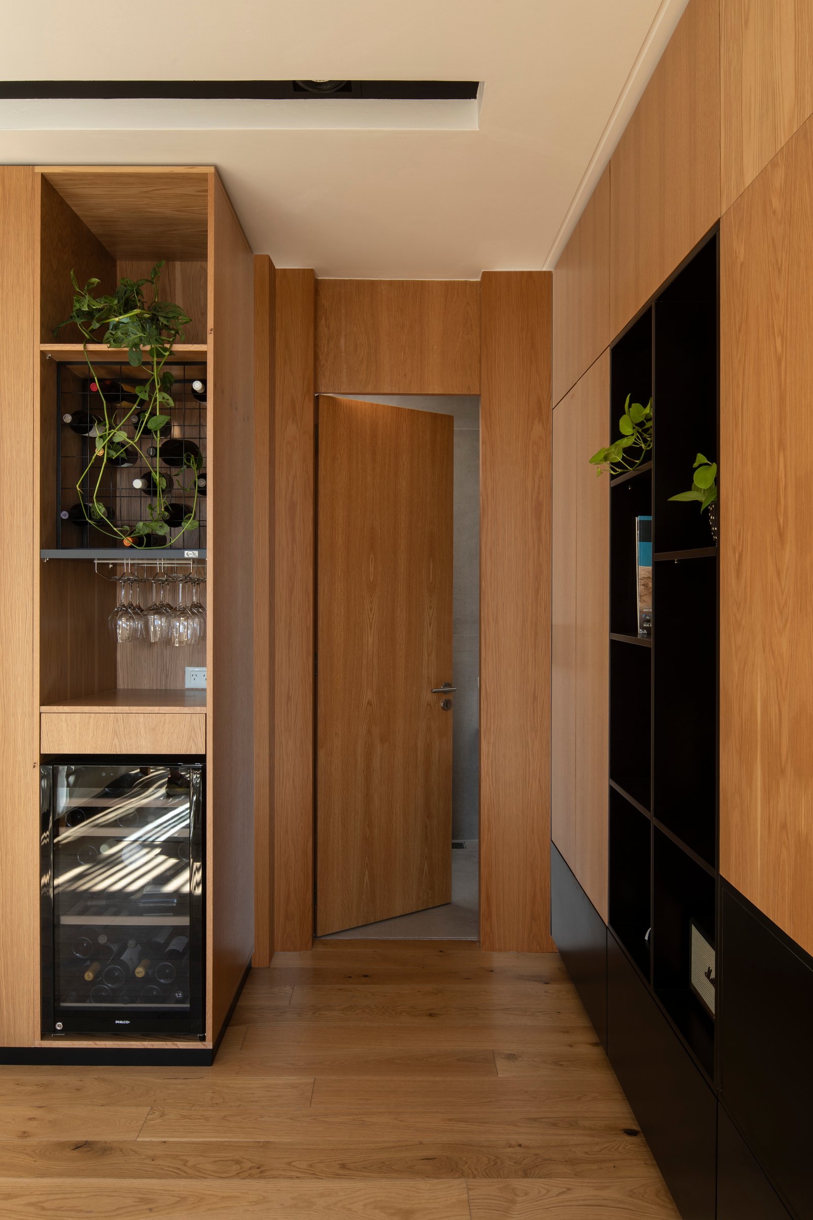 Pasillo moderno revestido en madera con cava integrada — proyecto Casa MECHA, por Grupo CRBN, en B1712 Castelar