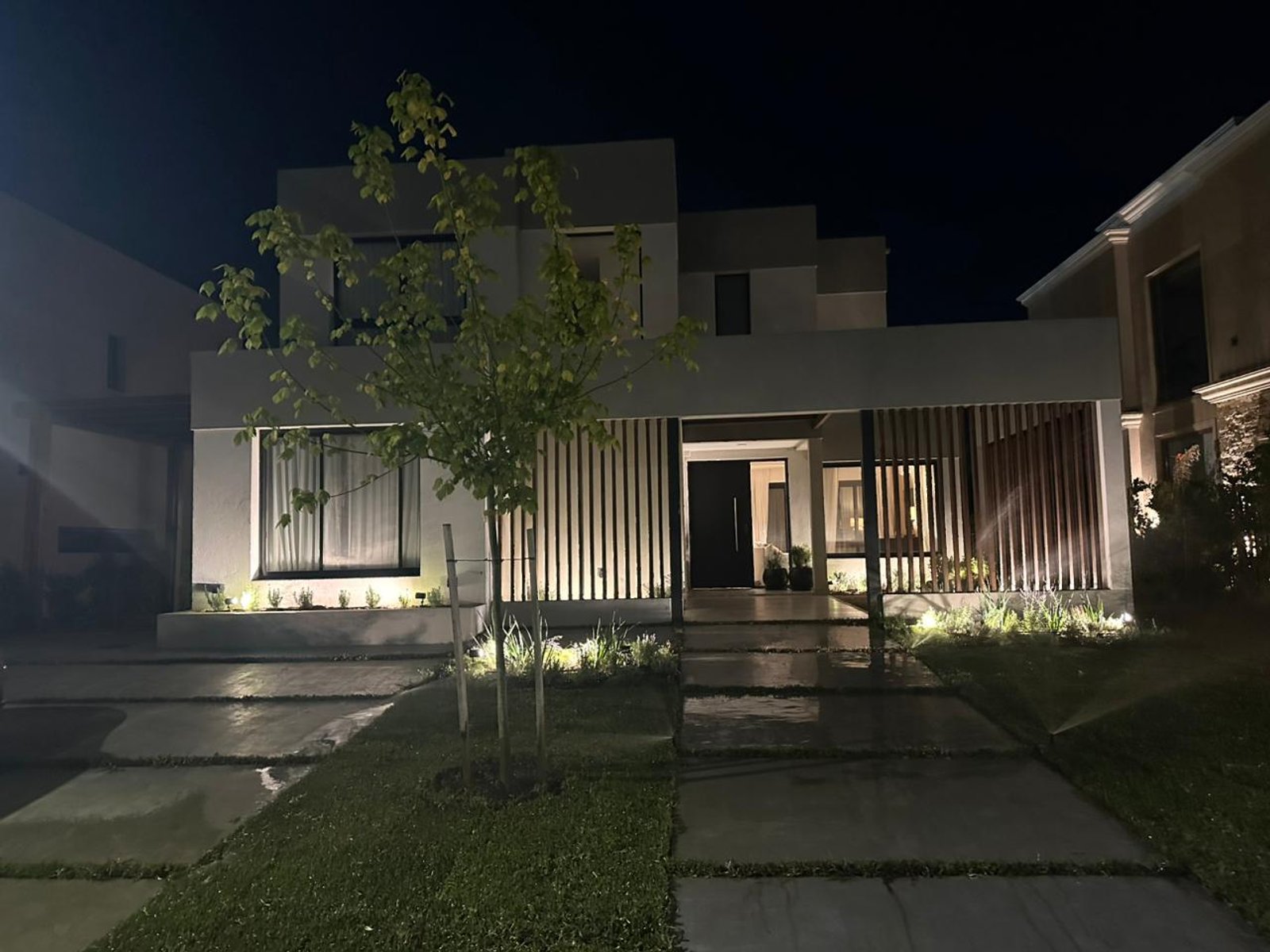 fachada moderna con iluminación cálida y amplios ventanales — proyecto CARPINCHOS, por Baires Green, en Nordelta