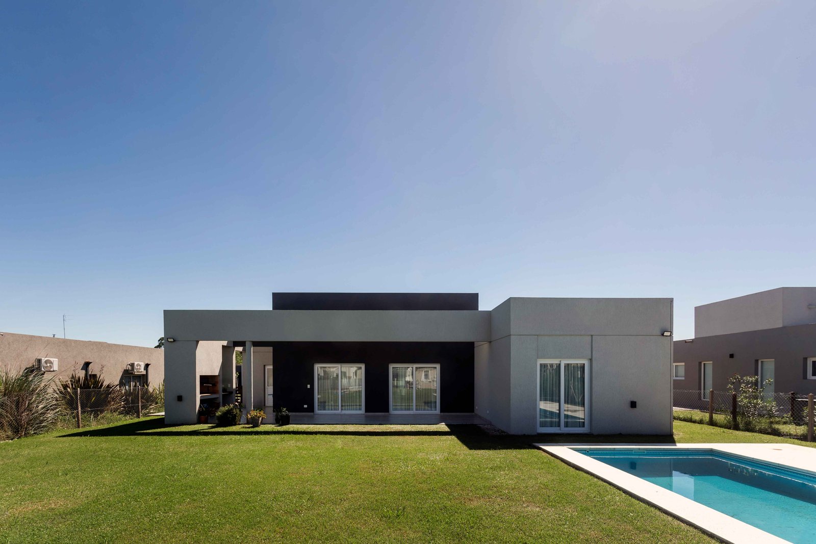 casa moderna gris con pileta y césped impecable — proyecto SANTA INÉS I, por Estudio Stepa, en Canning