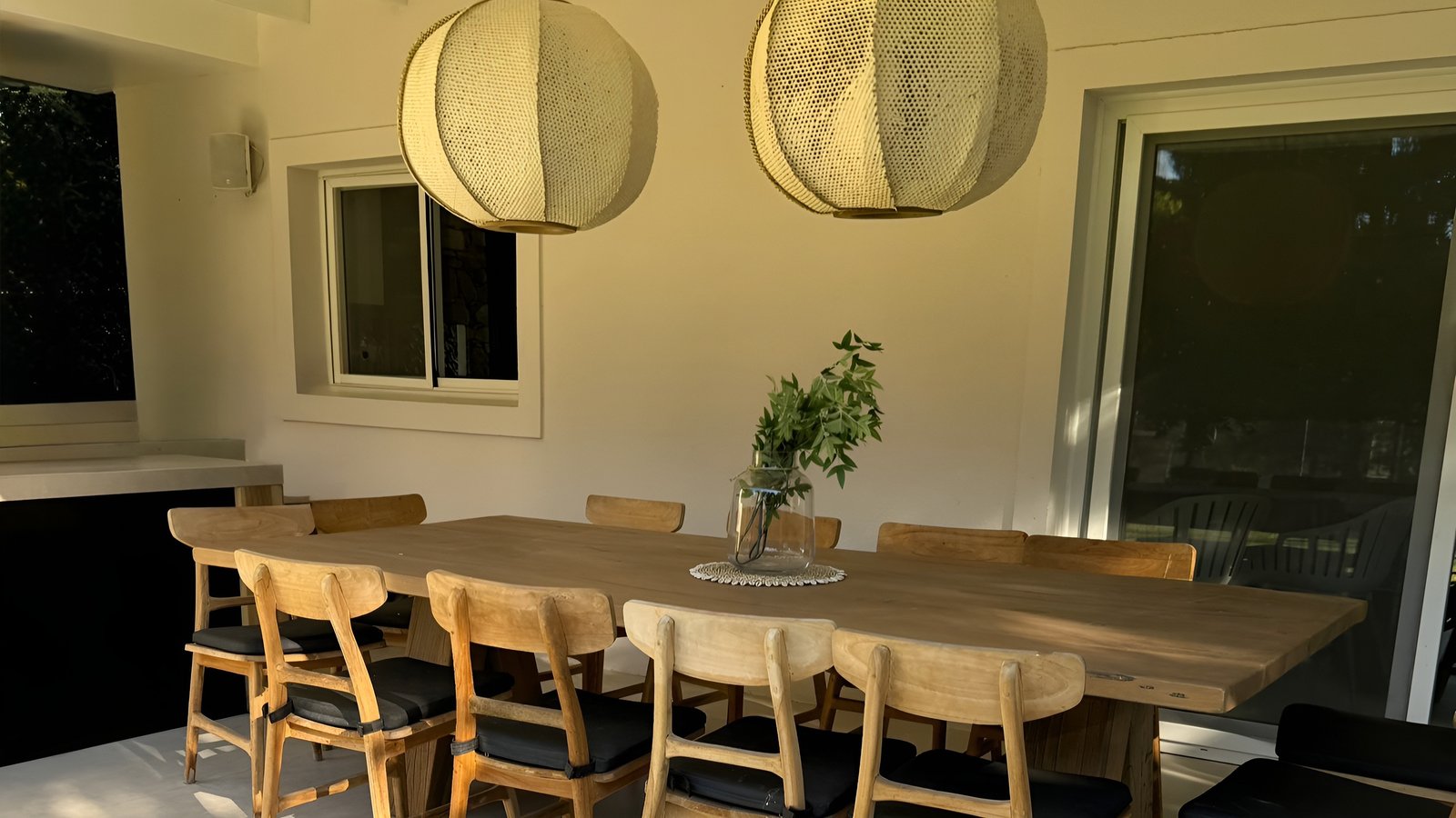 Comedor exterior moderno con mesa de madera y lámparas tejidas — proyecto Casa CC, por Hermann Arquitectos, en Los Castores
