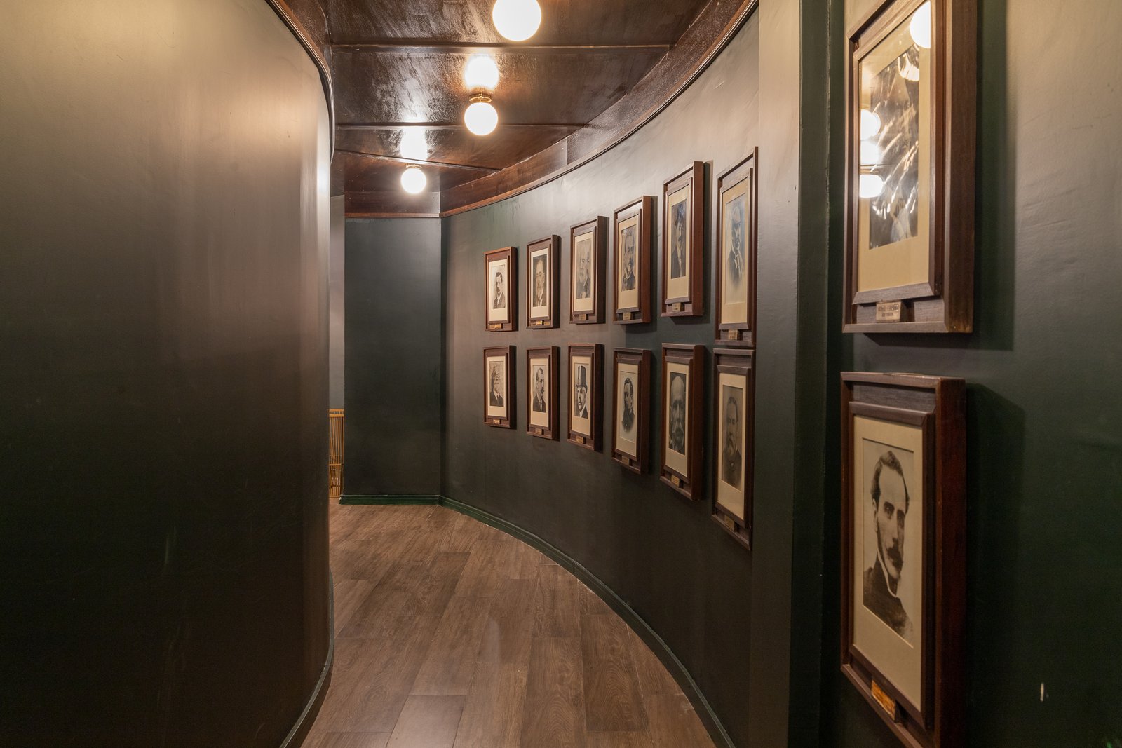 corredor curvo com galeria de retratos e teto de madeira — projeto PRESIDENTE BAR HIPODROMO, por AB ARQUITECTURA, em San Isidro