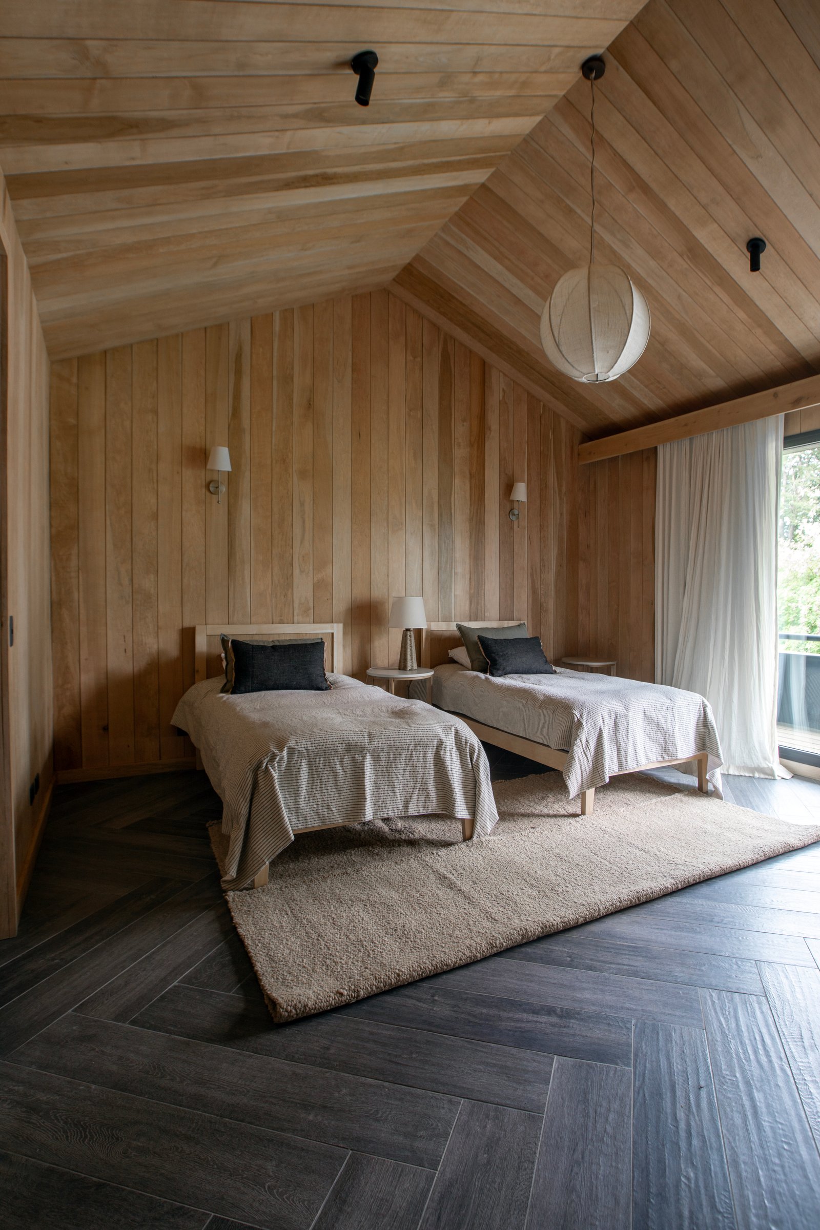 Dormitorio rústico con paredes y techo de madera, dos camas y lámpara colgante — proyecto OBRA SANTA BARBARA, por ILVA, en Provincia de Buenos Aires