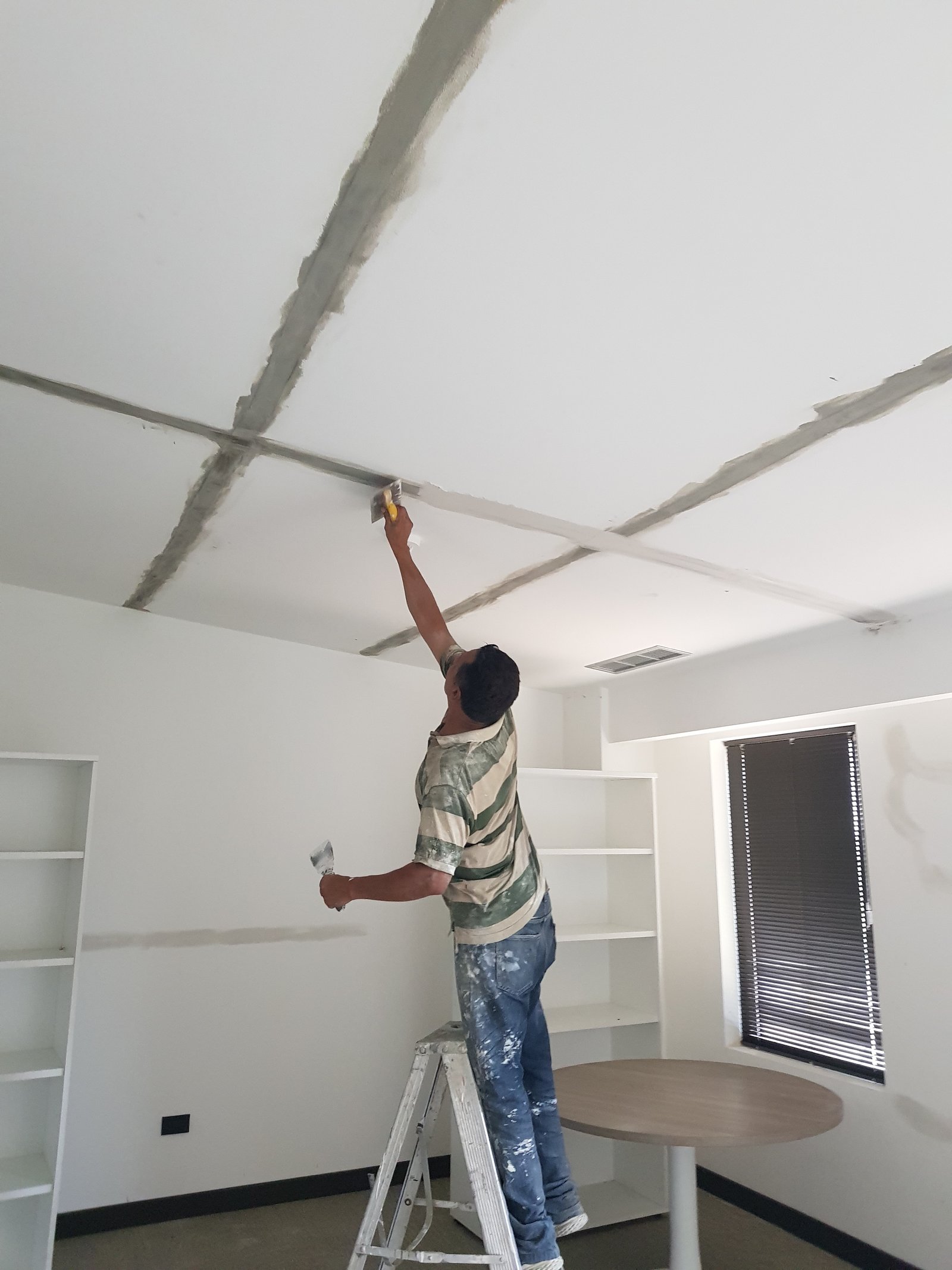construção de escritório: trabalhador aplicando massa no teto — projeto Montajes eléctricos en oficinas Comerciales, por Mantenimientos Comerciales Leon, em Buenos Aires