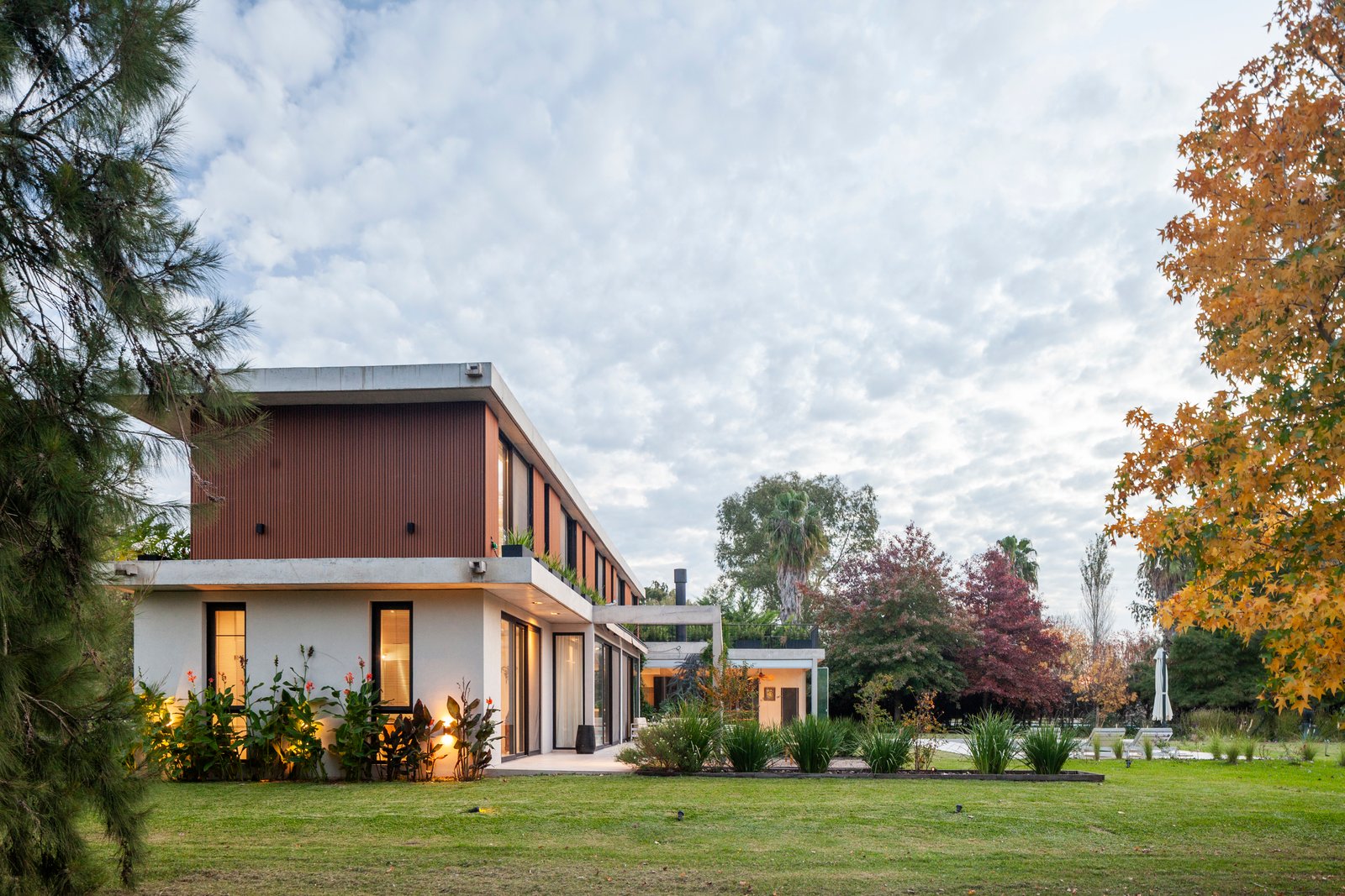 Fachada moderna con terraza de madera y vegetación exuberante — proyecto CASA HS143, por A'PRIMA - Arquitectura Sustentable, en km 7.5 Ruta 25