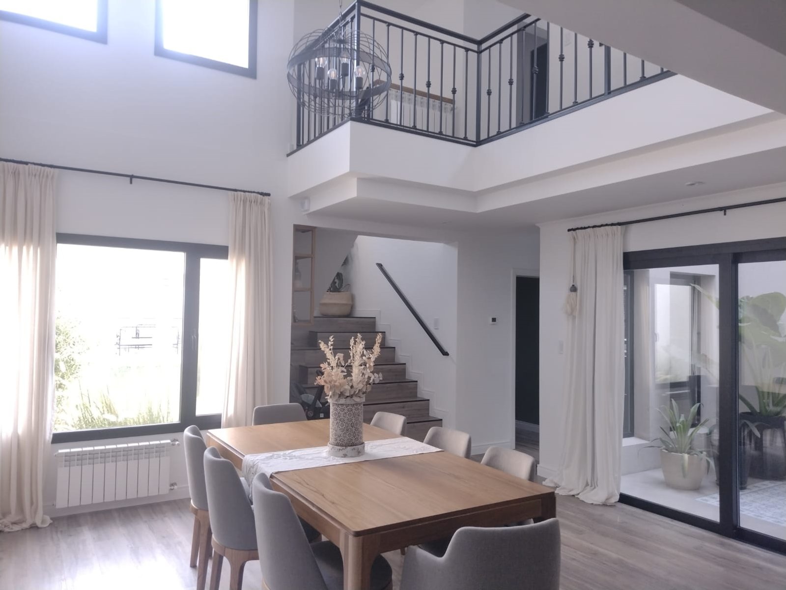 Comedor moderno de doble altura con grandes ventanales y escalera flotante — proyecto Casa FF, por Forma, en Balcarce
