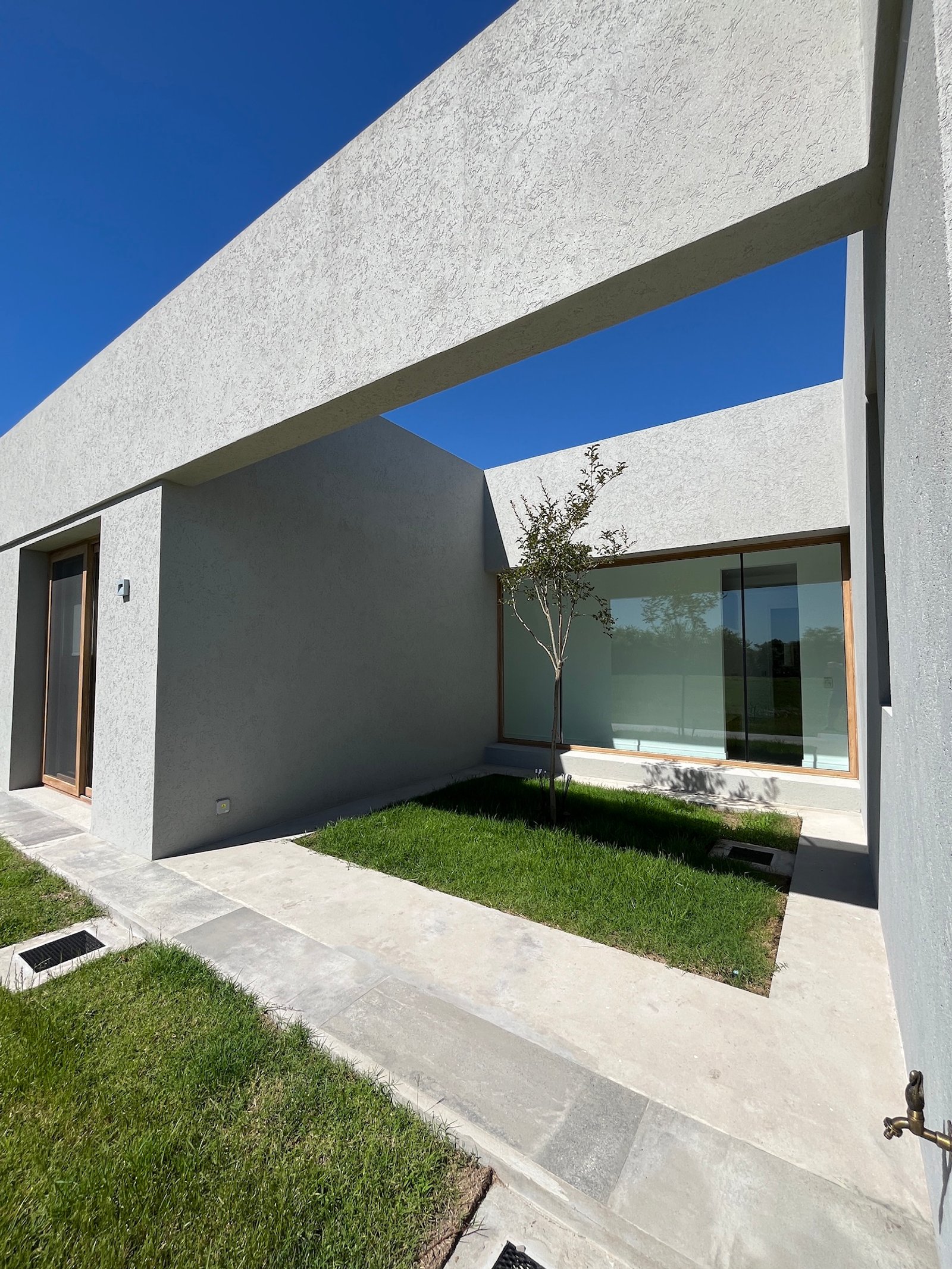 Fachada moderna con patio interior, hormigón texturizado y grandes ventanales — proyecto La Colina, por Arcucci Arquitectura, en La Colina Villa de Campo