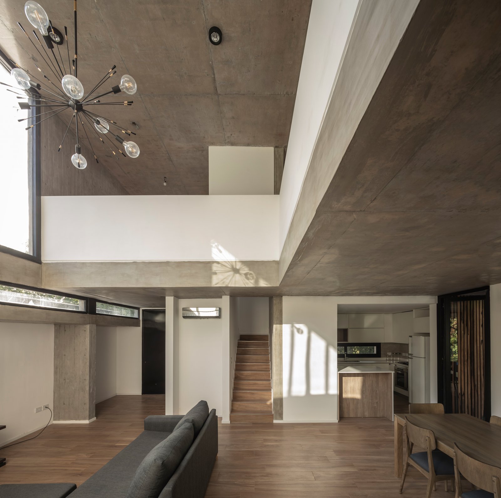 Living moderno con altura doble, hormigón visto y lámpara industrial — proyecto Casa Emilia, por Grupo CRBN, en Parque Leloir