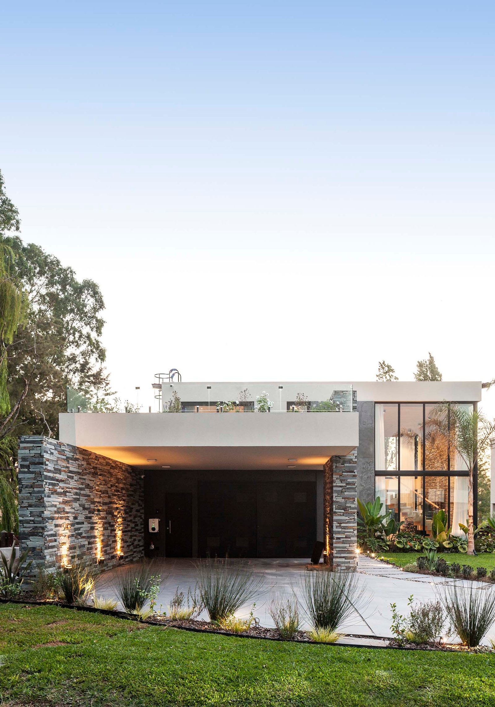 Fachada moderna com paredes de pedra e grandes janelas — projeto CASA T199, por A'PRIMA - Arquitectura Sustentable, em Los Robles 5901