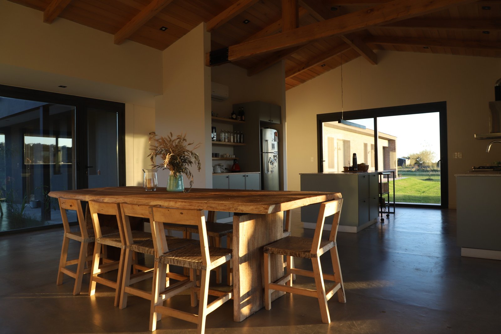 Comedor rústico de madera con vigas expuestas y mucha luz natural — proyecto Casa Areco, por R+B arquitectos, en San Antonio de Areco