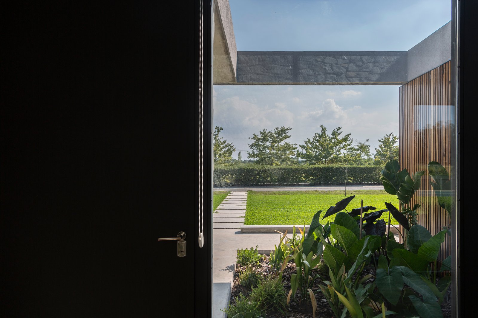 Pátio moderno com porta preta aberta e vegetação exuberante — projeto Casa Cruz, por Grupo CRBN, em B2812 Exaltación de la Cruz