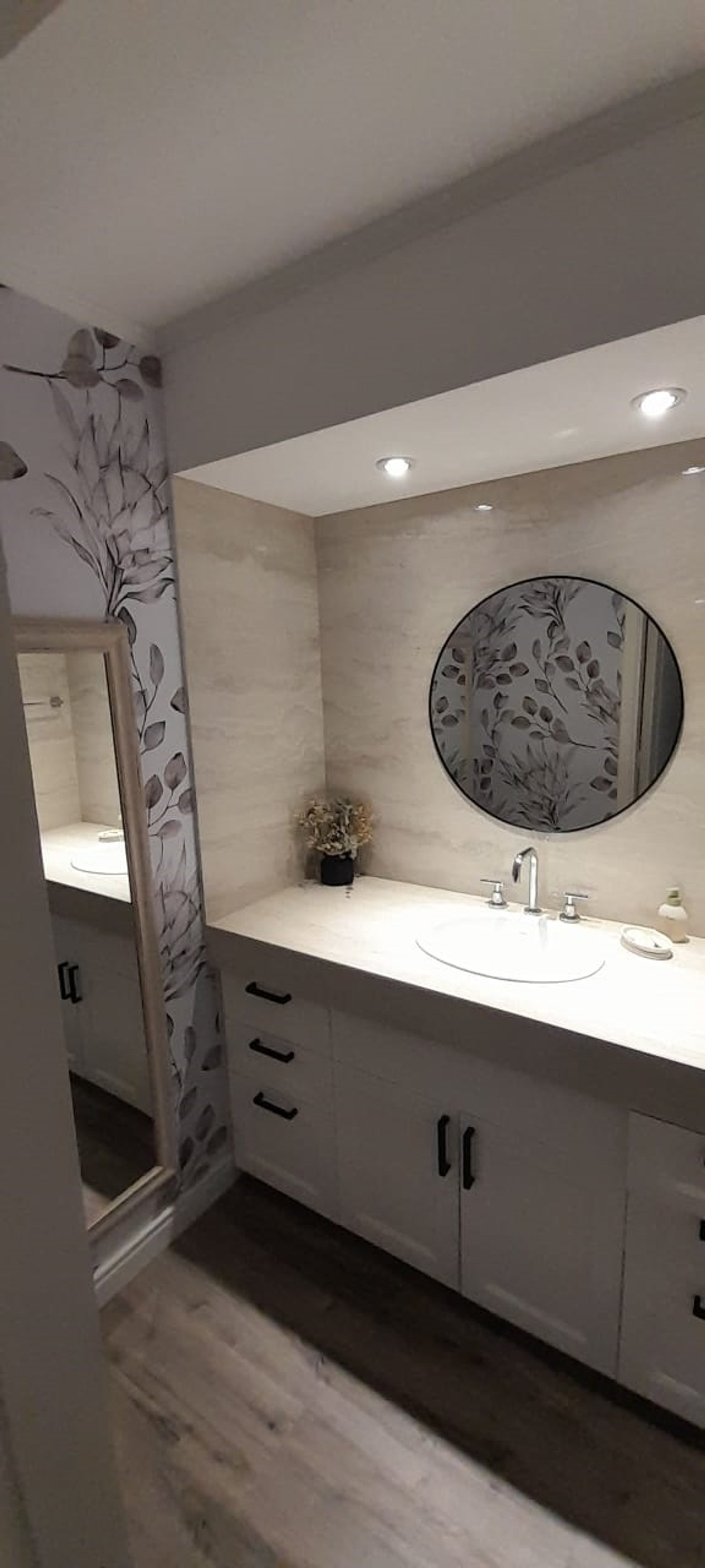 Baño moderno con tocador, lavabo ovalado, espejo redondo y papel tapiz botánico — proyecto Casa FF, por Forma, en Balcarce