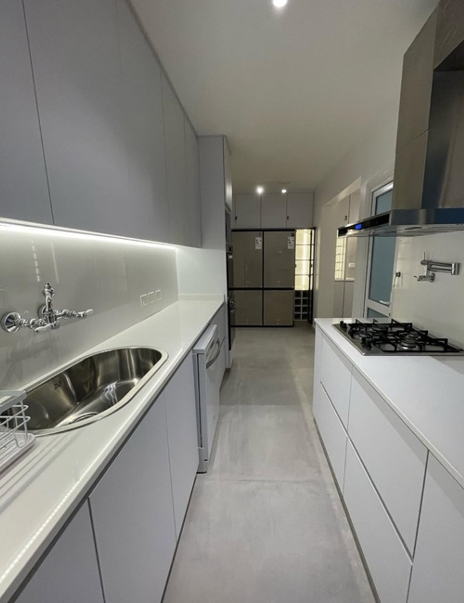 Cocina moderna lineal con gabinetes blancos y luz indirecta — proyecto Kennedy , por Estudio NET Arquitectura , en John Fitzgerald Kennedy