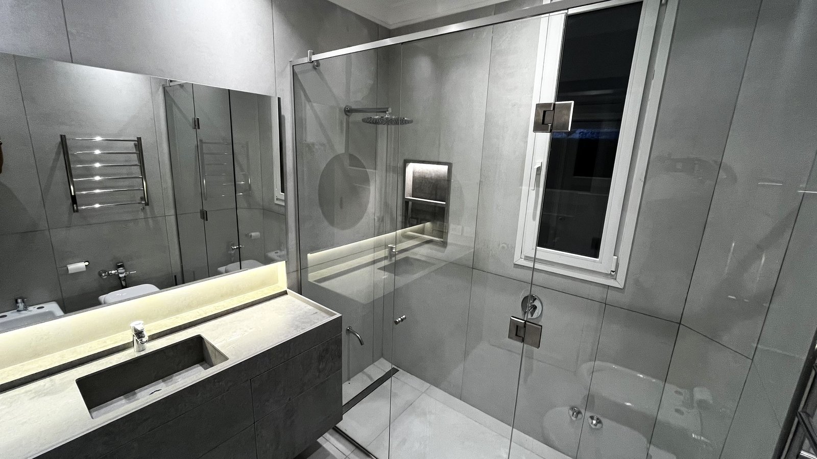 Baño moderno minimalista con ducha de cristal y revestimiento gris — proyecto CASA CERRITO (German Salas arquitectura), por German Salas arquitectura - San Isidro, en Buenos Aires