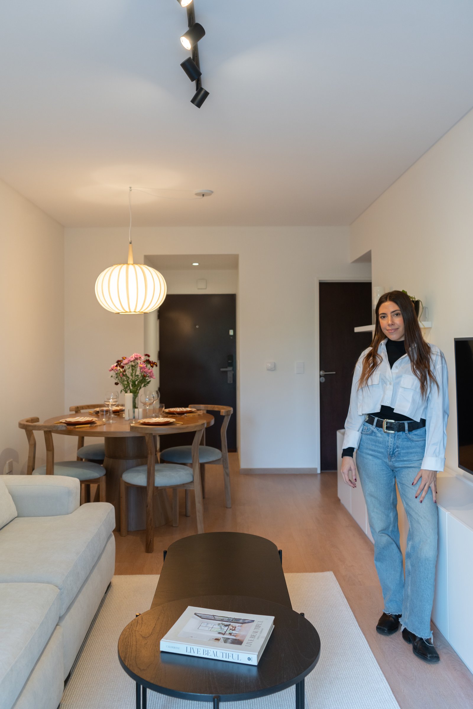 Living y comedor moderno abierto con sofá beige y mesa redonda de madera — proyecto Ugarte, por Estudio BDM, en Cdad. Autónoma de Buenos Aires