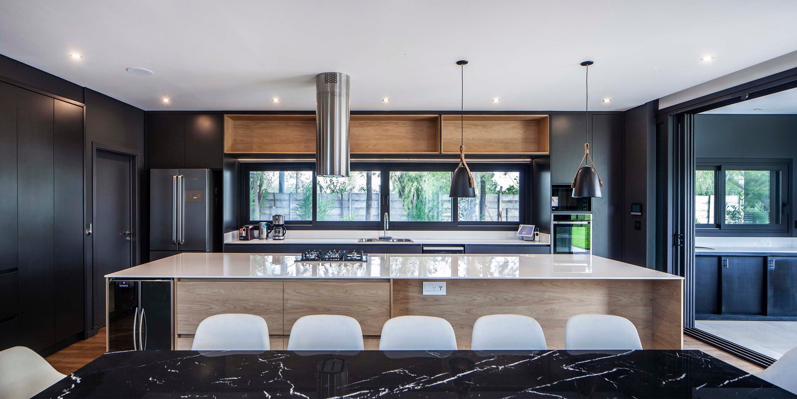 Cocina moderna con isla grande, paredes oscuras y detalles en madera — proyecto CASA T199, por A'PRIMA - Arquitectura Sustentable, en Los Robles 5901