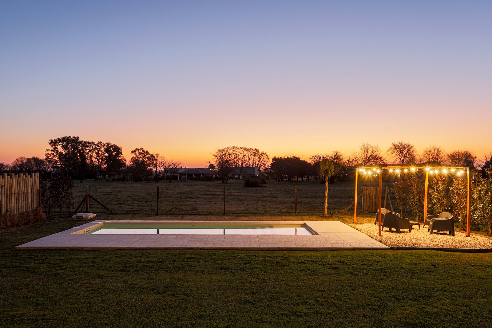 Piscina exterior moderna al atardecer con pérgola iluminada — proyecto SS45, por EZ architects, en Pilar