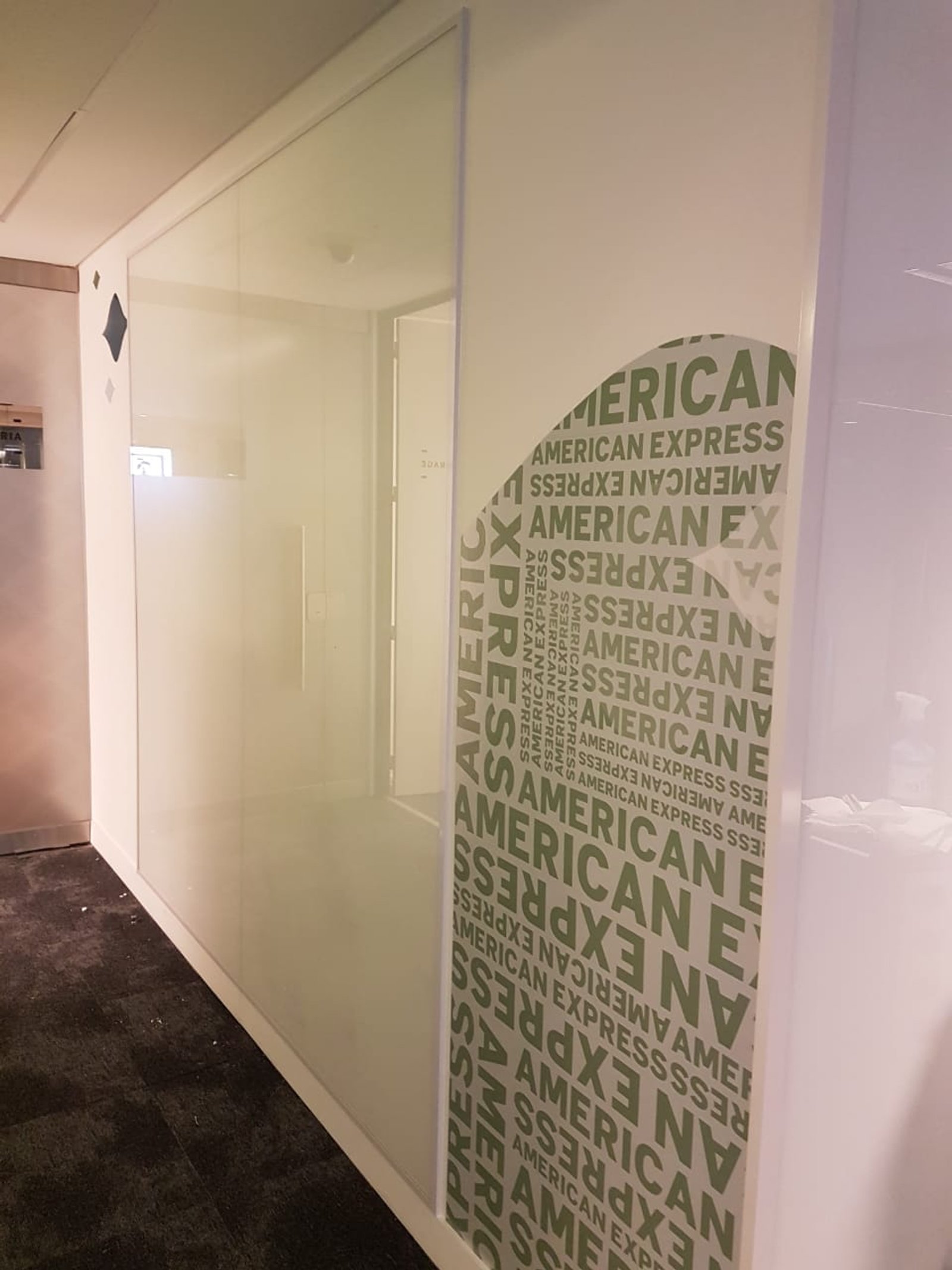 Interior de local comercial con patrón American Express en pared — proyecto Coverglass laminado 3+3 blanco, por Cristalcenter, en Retiro