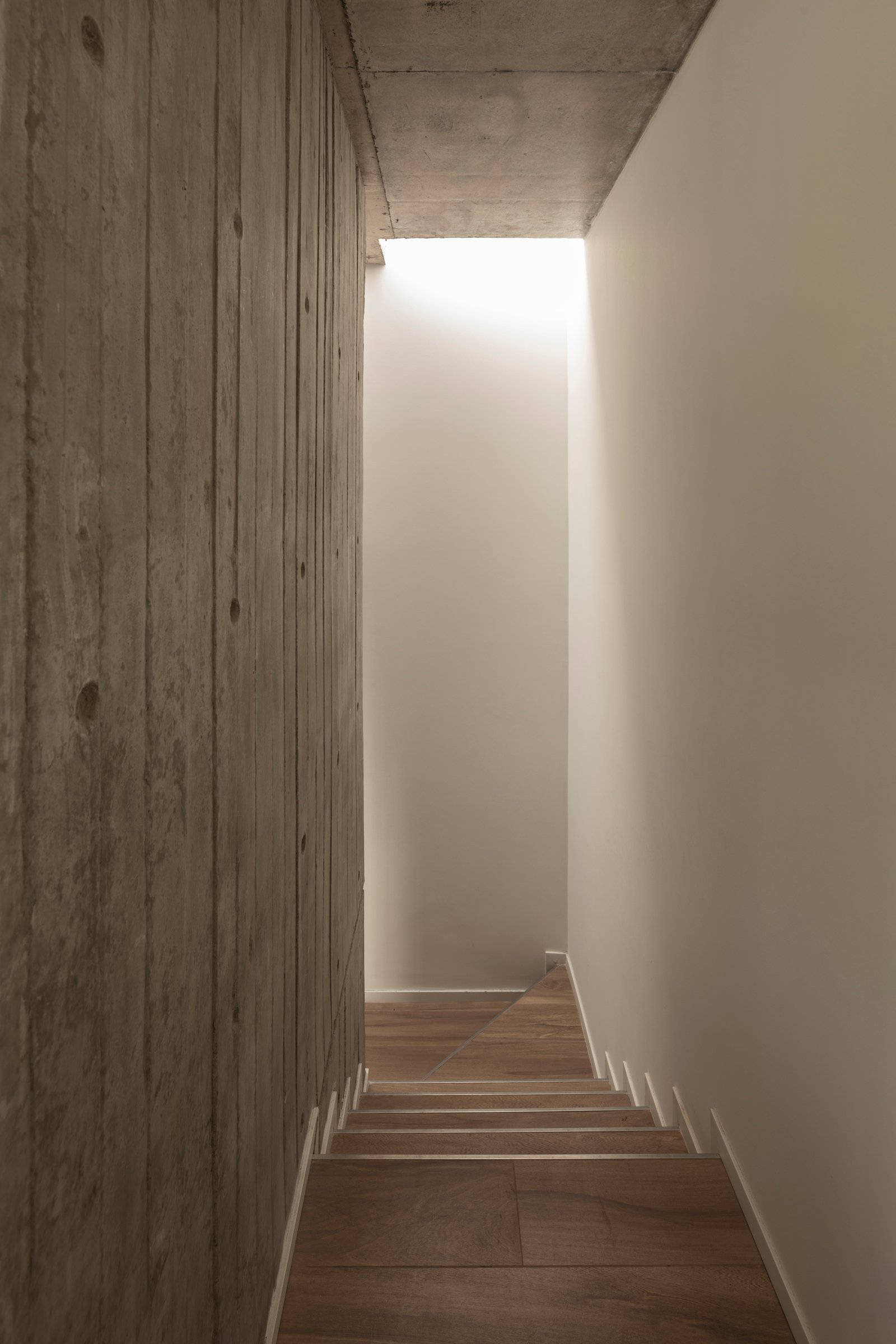 Pasillo moderno con muro de hormigón expuesto y escalera flotante — proyecto Casa Emilia, por Grupo CRBN, en Parque Leloir