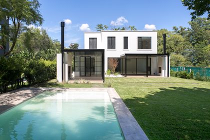 Casa moderna blanca con piscina y amplios ventanales en un entorno verde — proyecto Bosque Chico, por Estudio Arq. María Sioli, en Garin