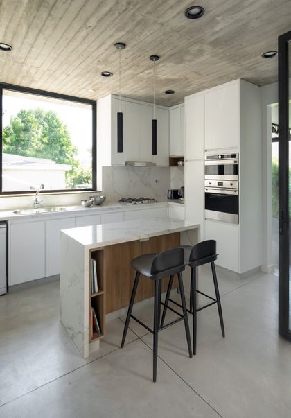 Cocina moderna con isla de mármol, techo de hormigón y ventanas grandes — proyecto Casa PVTM, por Estudio Lak, en Barrio Laguna del Sol