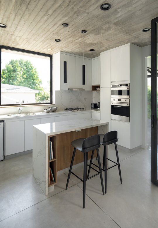 Cocina moderna con isla de mármol, techo de hormigón y ventanas grandes — proyecto Casa PVTM, por Estudio Lak, en Barrio Laguna del Sol