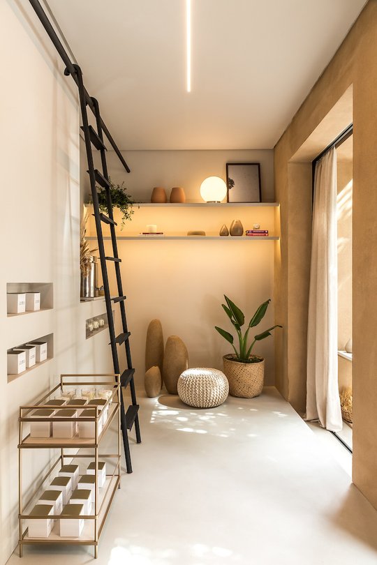 Espacio comercial con estantes iluminados, escalera decorativa y objetos de diseño — proyecto Esmo, por Boscardin Corsi Arquitetura