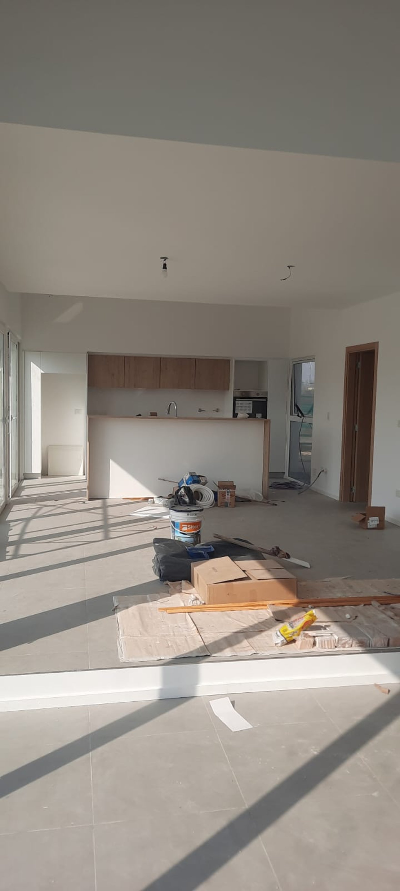 Cozinha e sala em construção, iluminação natural abundante, piso cinza — projeto Aires, por ECSA, em Mar de Ajó
