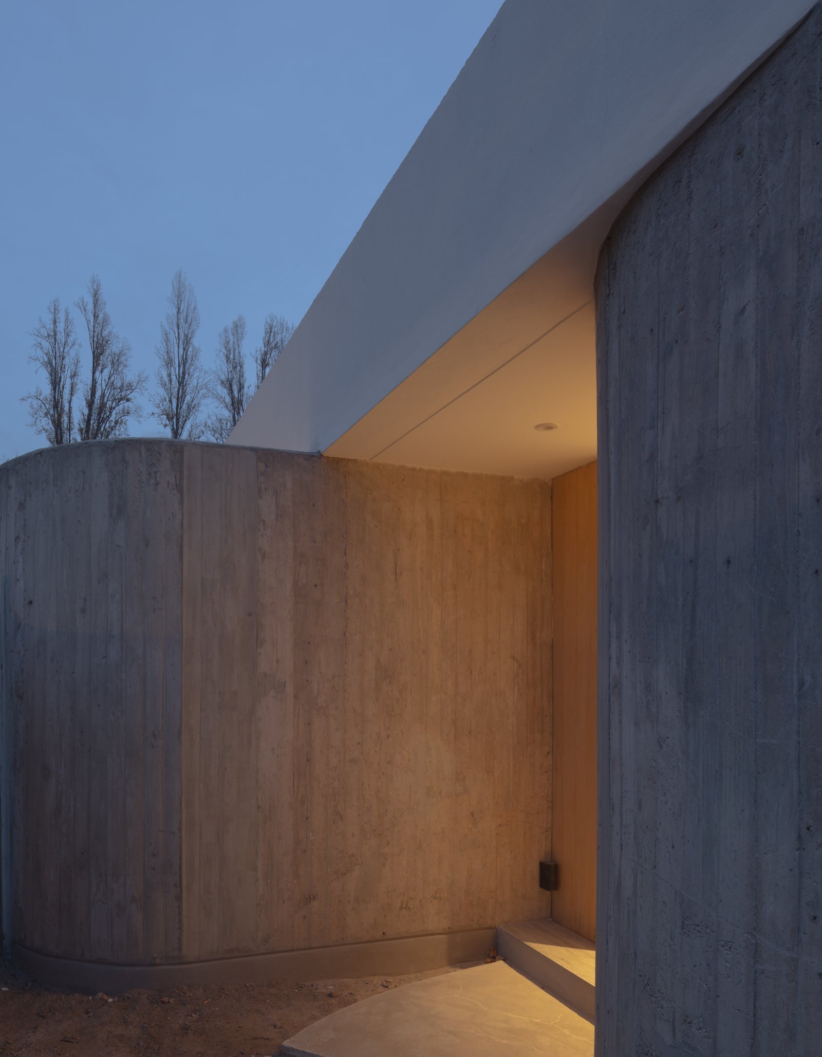Fachada moderna de concreto com paredes curvas ao entardecer — projeto Vivienda CCE, por ONA - Oficina Nómada de Arquitectura, em M5505 Chacras de Coria