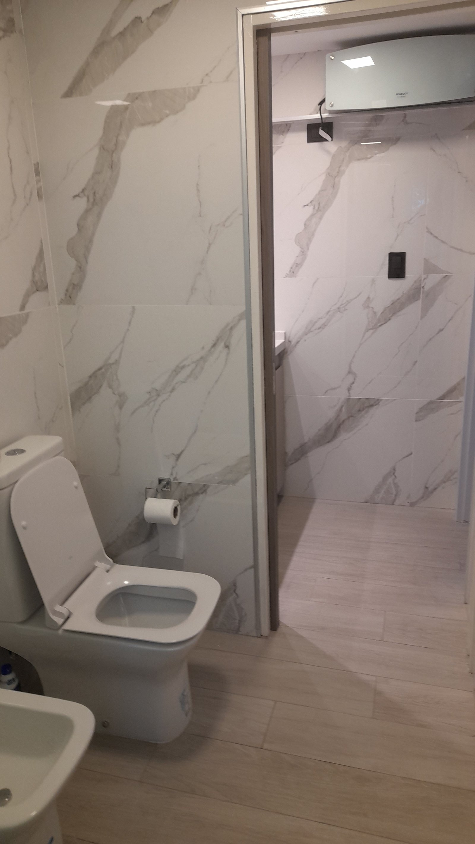Banheiro moderno com paredes de mármore e piso de madeira — projeto Remodelación de baño, por CN Construcciones, em Alta Gracia