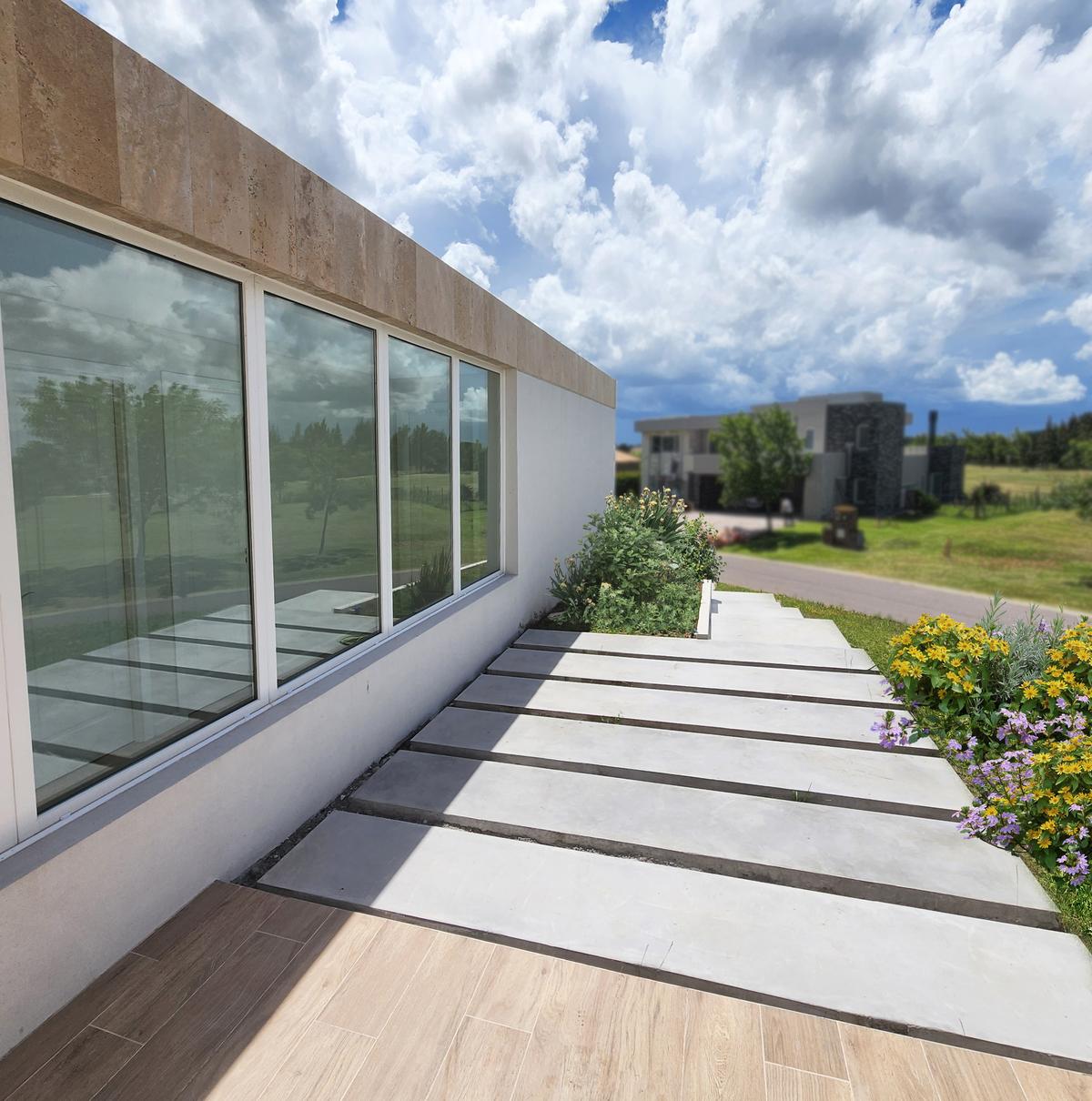 Fachada moderna com grandes janelas e caminho de lajes de concreto — projeto Casa Cardales, por Hernan Goldfarb, em Belén de Escobar