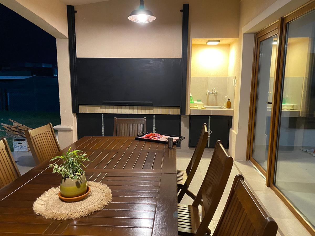 Sala de jantar externa de madeira sob pergolado com plantas — projeto Casa El Rebenque, por Arq. Leonardo  De Lorenzi, em Canning