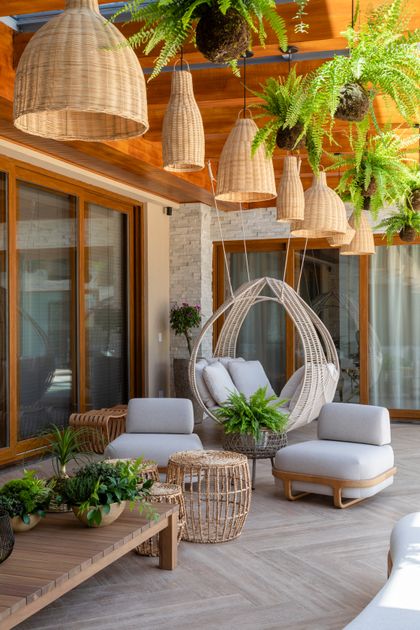 Terraza semiexterior con deck de madera, luces colgantes y sillas de ratán — proyecto Projeto Destaque Club&Casa, por OKA ARQUITETURA