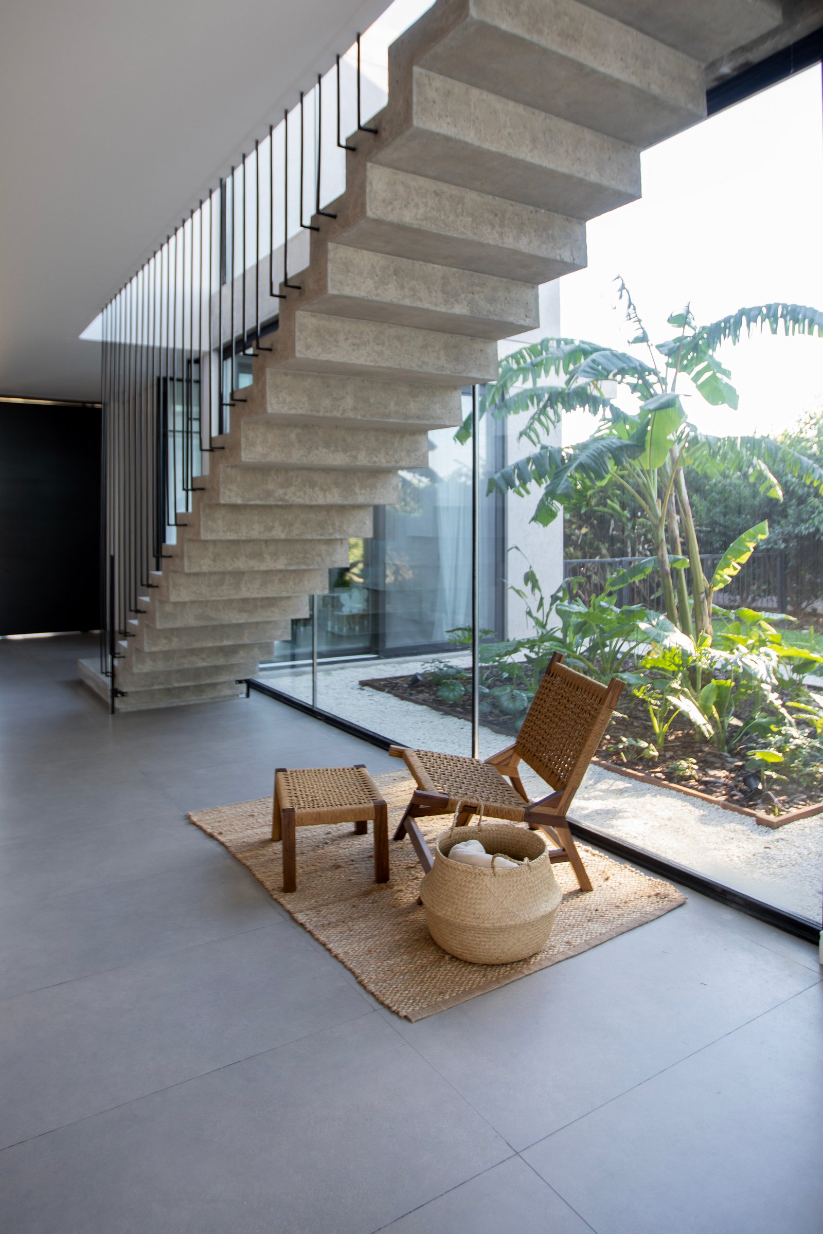 Escalera flotante de concreto con jardín exuberante y muebles de ratán — proyecto CASA TRIBECA CONCRETE BROADWAY, por ILVA, en Provincia de Buenos Aires