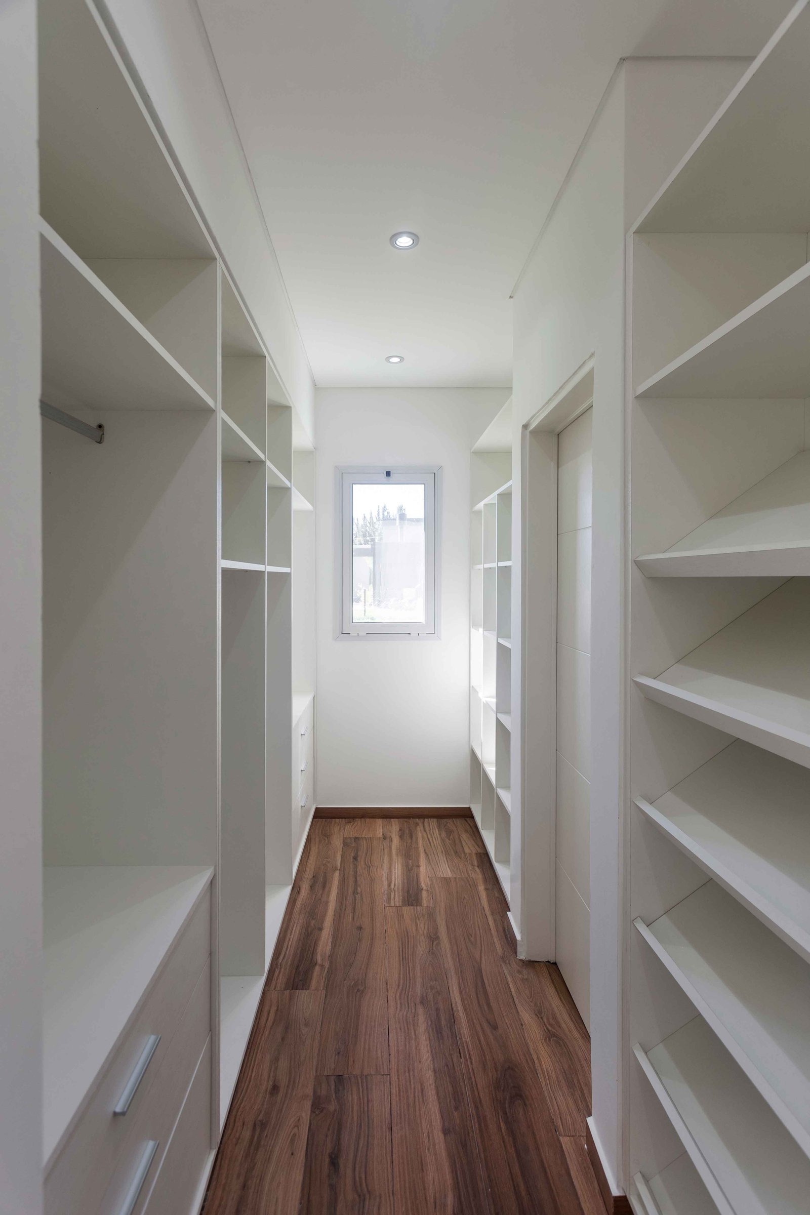 Corredor de closet moderno com prateleiras brancas e piso de madeira — projeto San Felipe, por Estudio Stepa, em Canning