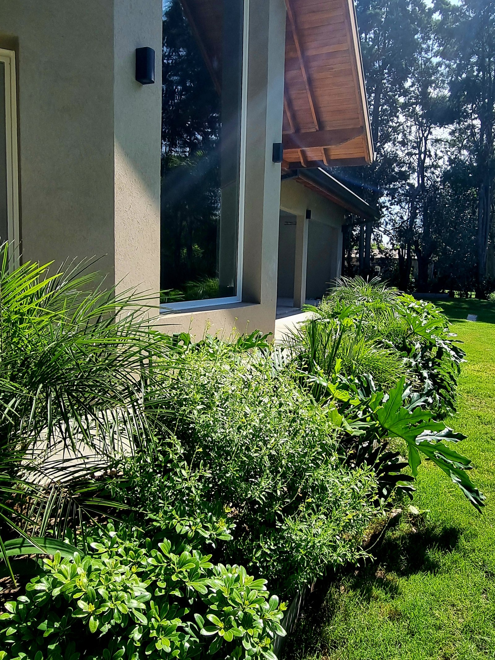 Fachada moderna com janela do chão ao teto e vegetação exuberante — projeto La Quinta, por Marcela García Brünner Paisajista, em El Pato
