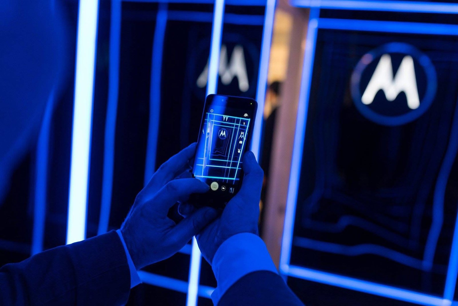Persona con celular frente a luces azules y logo — proyecto Espacio Motorola, por DE DIOS Estudio, en Martínez