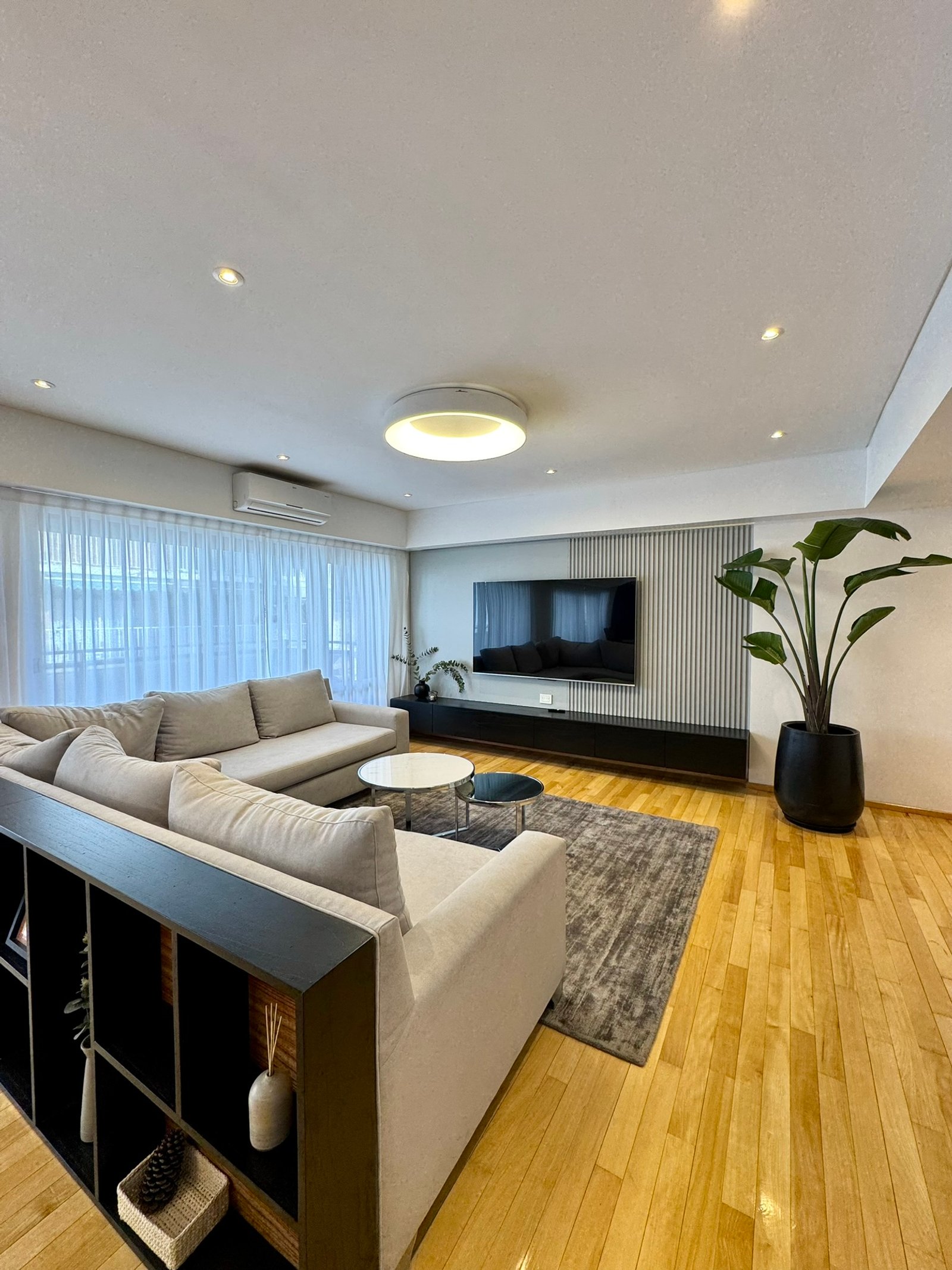 Sala de estar moderna com sofá modular bege, prateleiras embutidas e piso de madeira — projeto Mendoza, por MDBK Arquitectura, em Belgrano