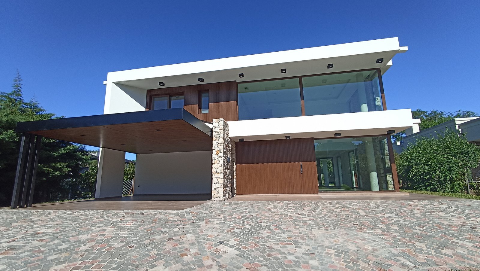 Fachada moderna de casa con grandes ventanales y detalles en madera y metal — proyecto Vivienda en Fincas de Hudson, por Monarq Arquitectura, en C. 137 7400