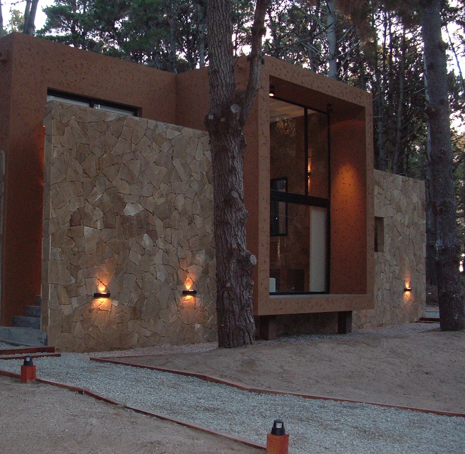 Fachada moderna com pedra, árvores e luz quente — projeto LA  ALHAMBRA, por GJF estudio, em Costa del Este