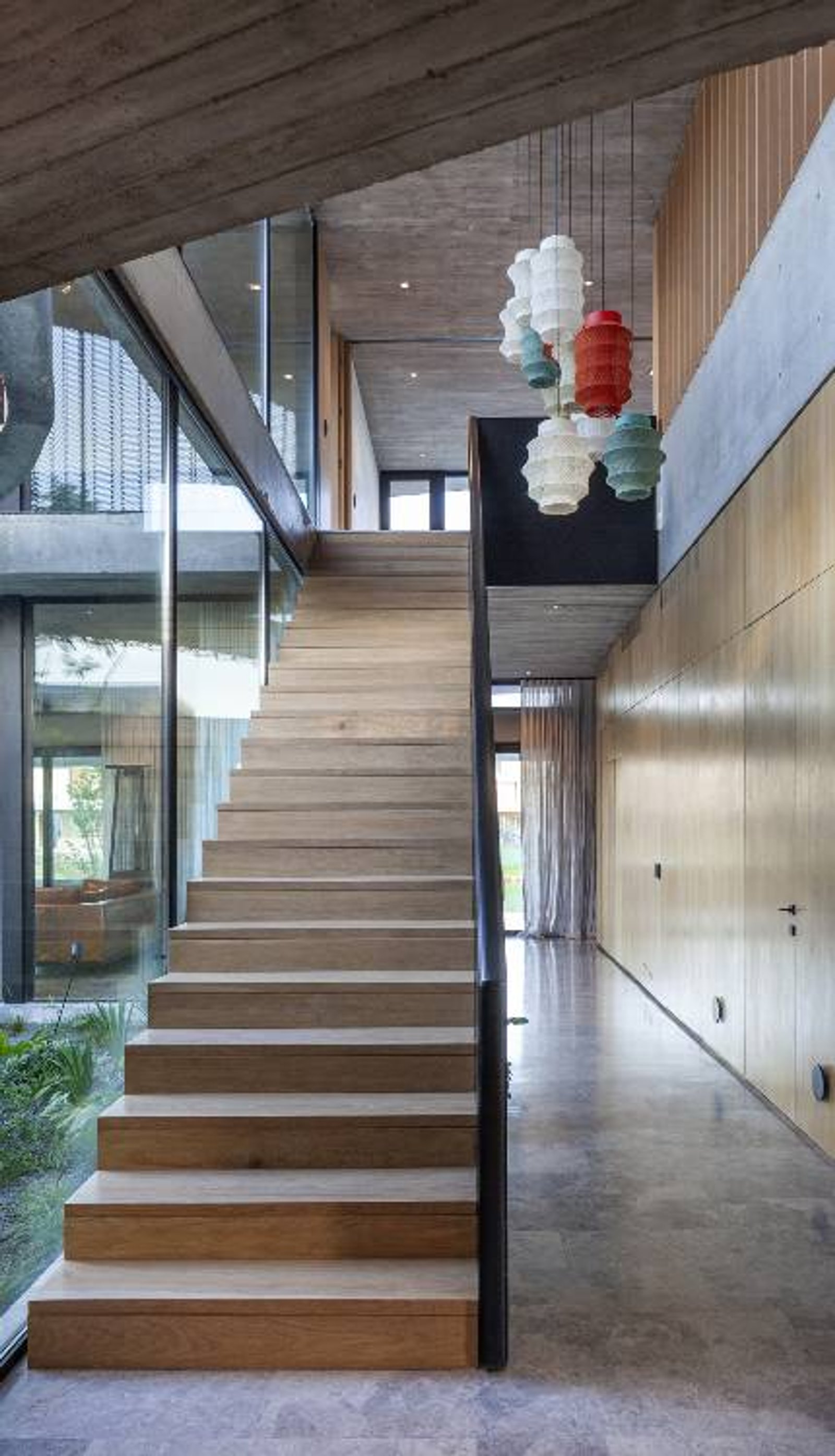 Escalera moderna de madera y hormigón con luces colgantes — proyecto Casa Órbita, por Estudio PK, en Nordelta