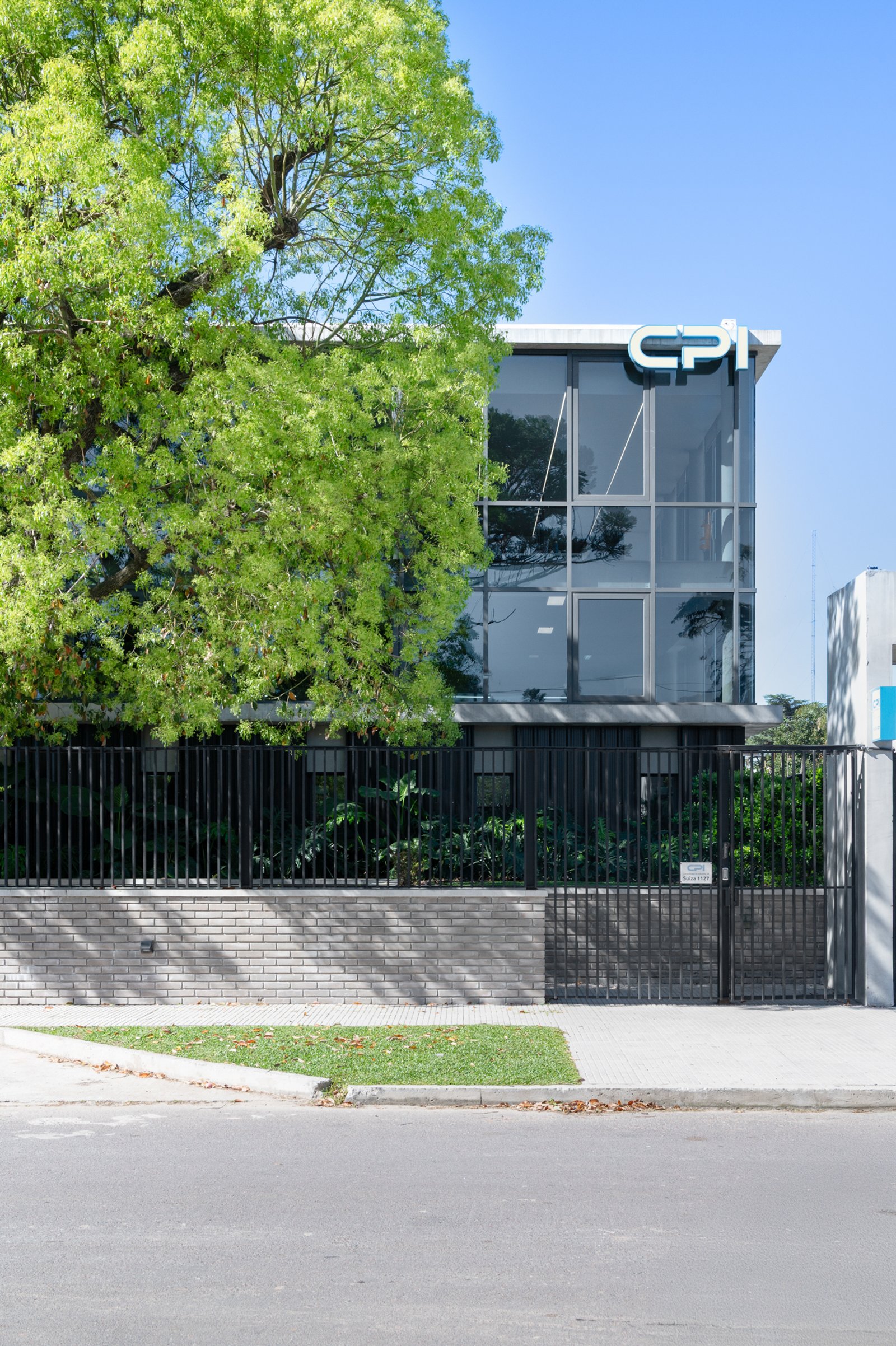 Edifício moderno com árvores exuberantes e fachada de vidro — projeto Oficinas CPI, por Juarez-Fevre Estudio de Arquitectura, em Provincia de Buenos Aires