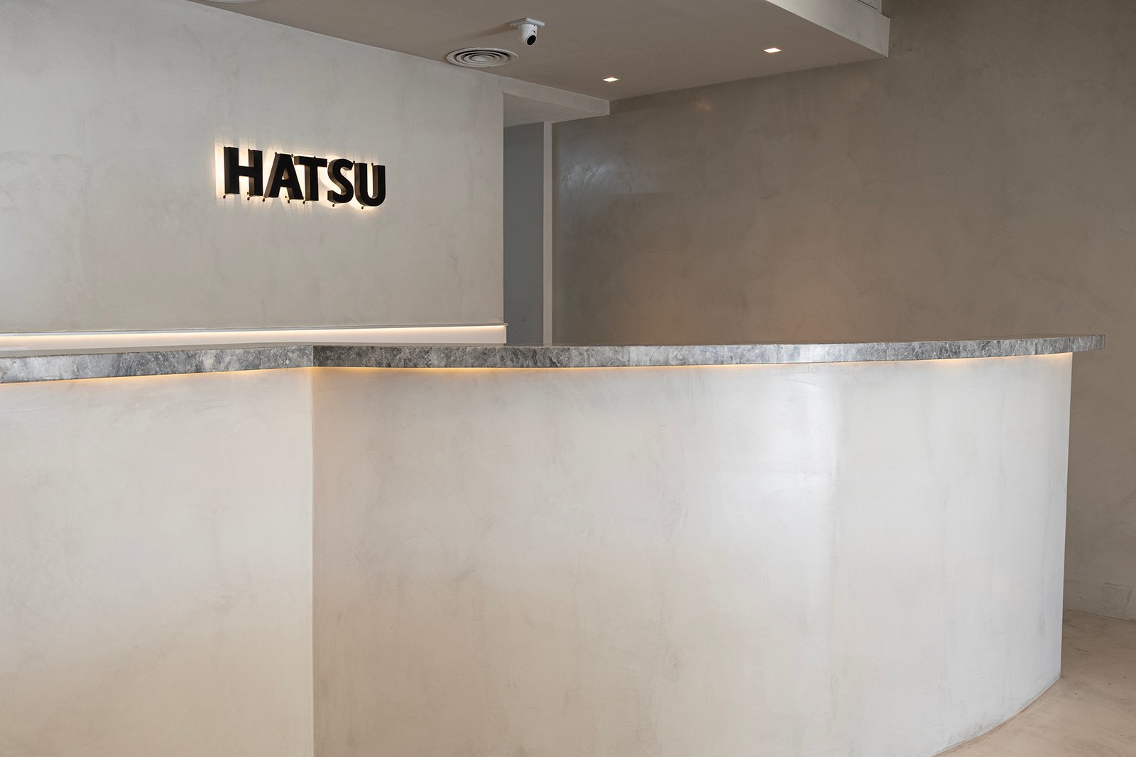 Recepción moderna con mostrador curvo de microcemento blanco y letrero iluminado — proyecto HATSU Núñez - MZV Arquitectura, por Gaby Alfonso, en Buenos Aires