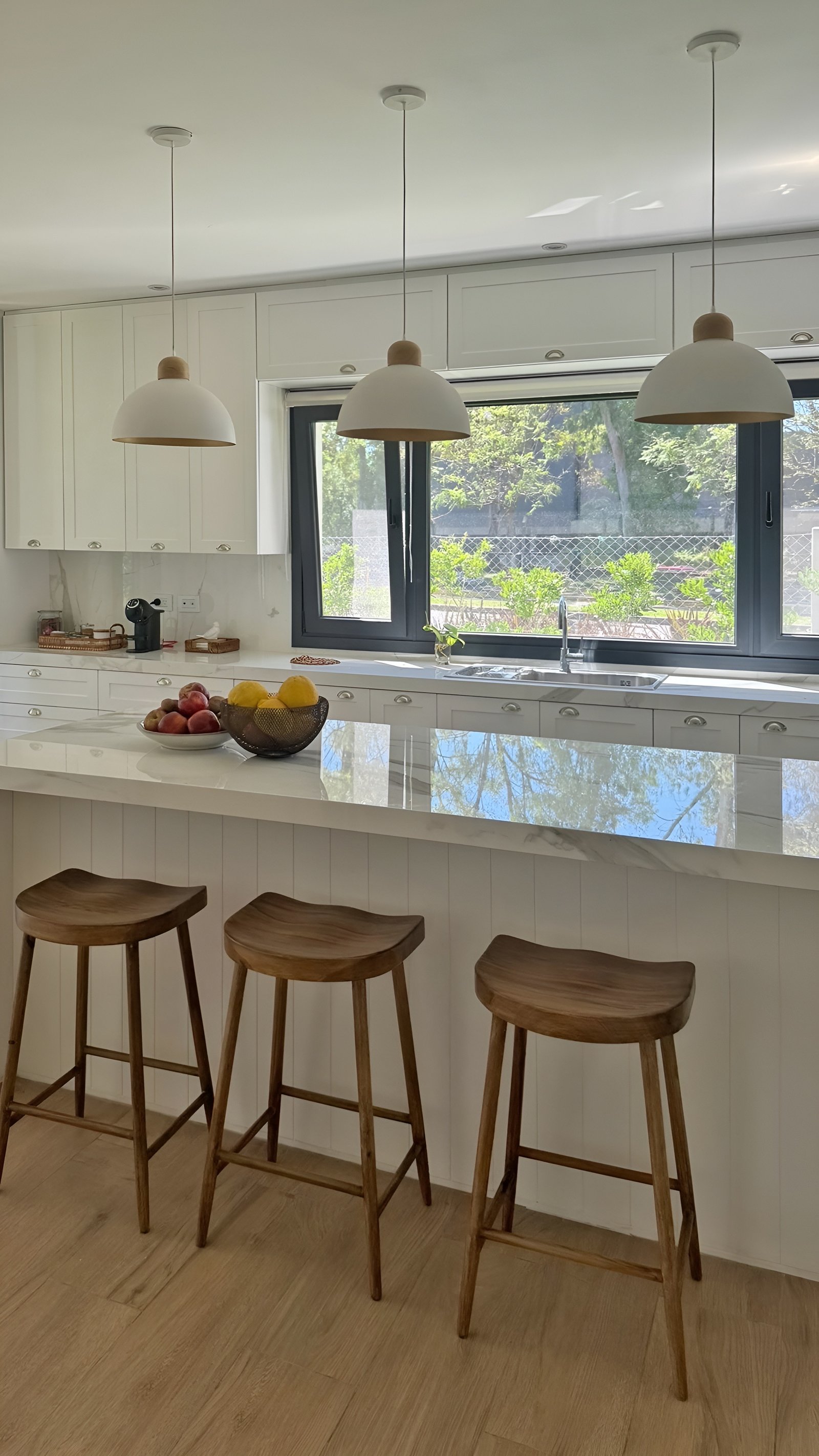 Cocina escandinava con isla de mármol, luces colgantes y taburetes de madera — proyecto Casa MC, por Hermann Arquitectos, en Bv. Central