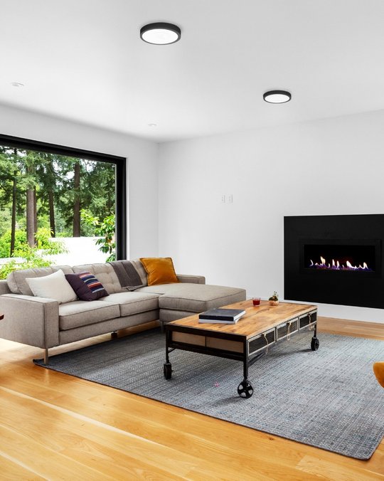 Living moderno con vista a bosque, sofá seccional y chimenea — proyecto Iluminamos tu futuro, por MACROLED