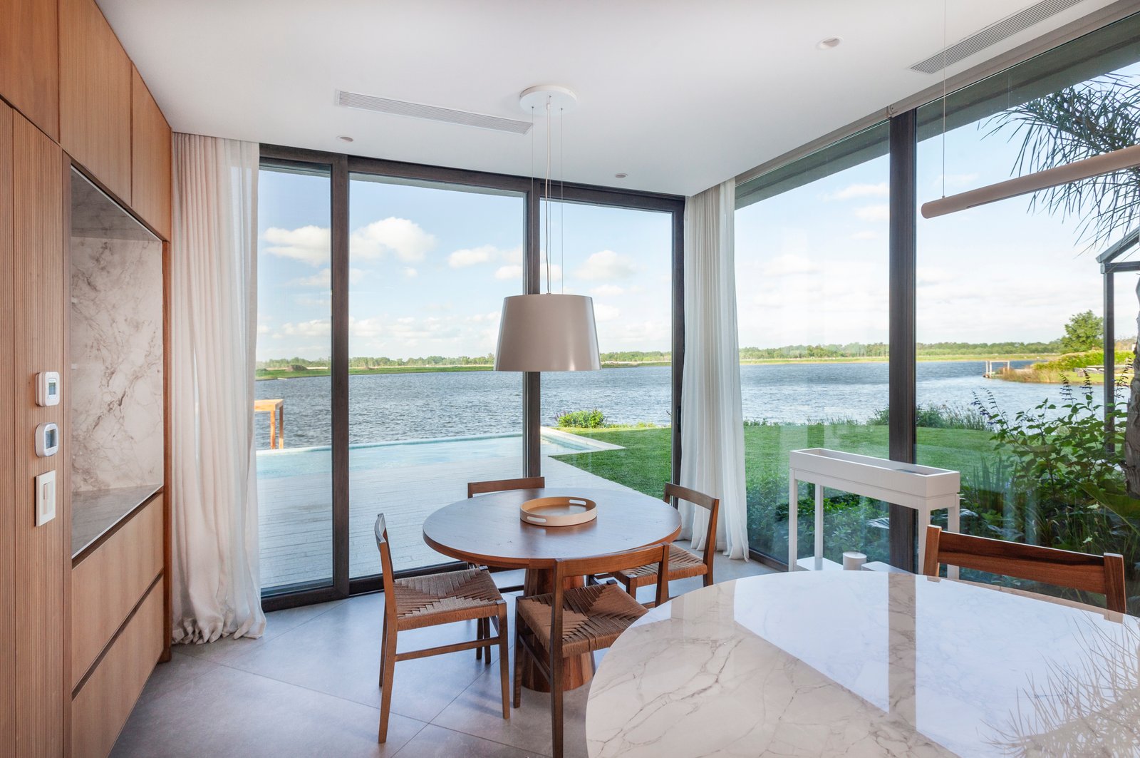 Sala de jantar moderna com vista para a água e detalhes em madeira — projeto CASA M40, por A'PRIMA - Arquitectura Sustentable, em Unnamed Road
