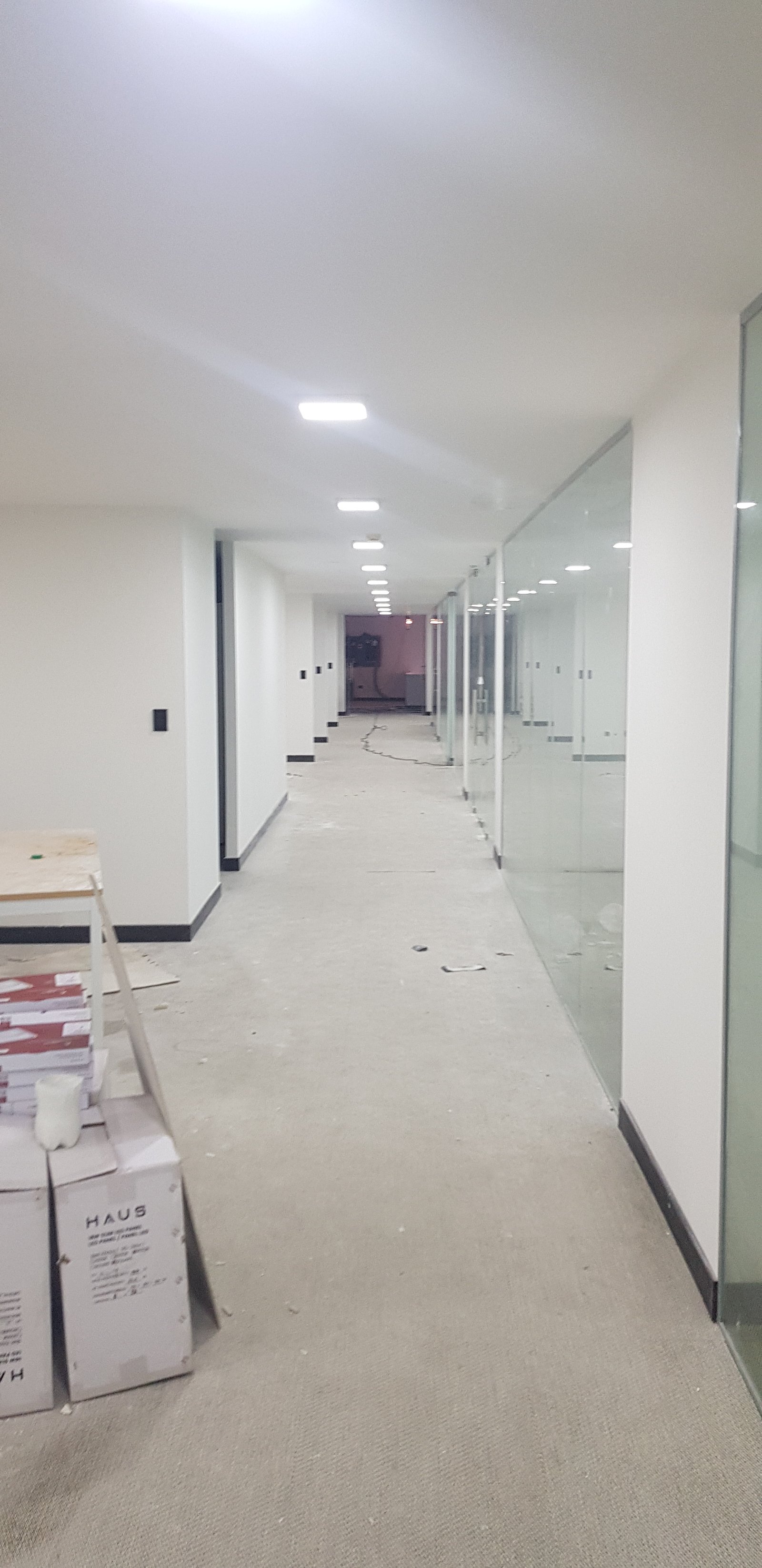 pasillo de oficina en construcción con paredes de vidrio y hormigón — proyecto Montajes eléctricos en oficinas Comerciales , por Mantenimientos Comerciales Leon , en Buenos Aires